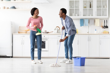 Cheerful black man and woman having fun while cleaning kitchen