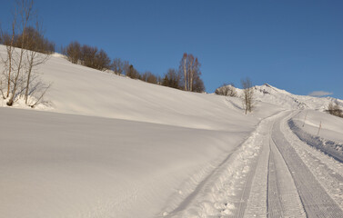 Fototapeta na wymiar snowy footpath crossing alpine mountain under blue sky