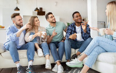 Group of happy millennial friends drinking tea, having talk, enjoying time together at home