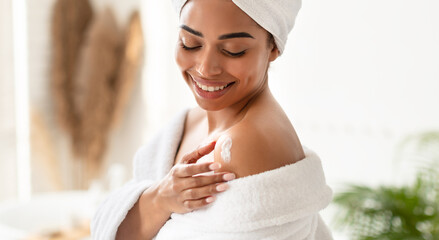 Black Young Woman Applying Moisturizer Cream On Shoulders In Bathroom
