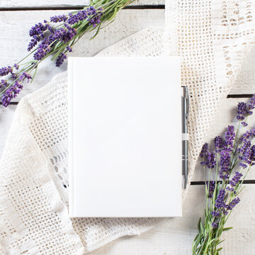 Blank white book with lavender flower frame on white lace and rustick wooden plank