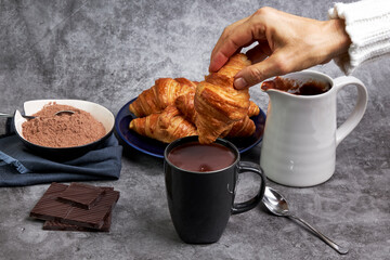 Hand of woman dipping a croissant in a cup of hot chocolate