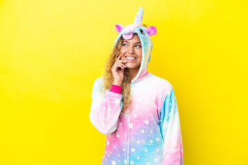 Girl with curly hair wearing a unicorn pajama isolated on yellow background thinking an idea while looking up