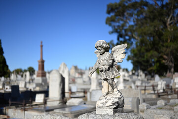 Stone sculpture of an infant angel, or cherub, mournfully scattering flowers in a cemetery on a sunny day