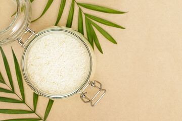 Rice grain in a glass bowl and palm leaves on a craft background