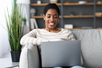 Millennial Black Lady Sitting On Couch With Laptop At Home