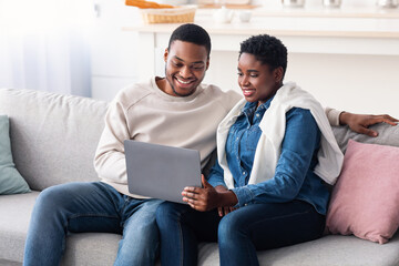African american couple sitting on couch, using laptop