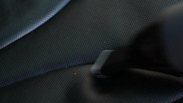 Cleaning crumbs from a perforated black leather car seat with a compact vacuum cleaner