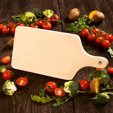 Wooden cutting board on rustic old plank with vegetables decoration.