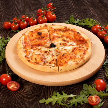 Pizza on wooden board placed on old rustic plank with vegetable and spice decoration. Restaurant menu.