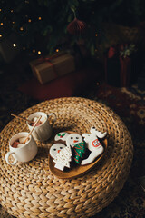 Obraz na płótnie Canvas Cocoa with marshmallow, paper straw and gingerbread on wicker table with Christmas tree on the background. Holiday festive decorations.