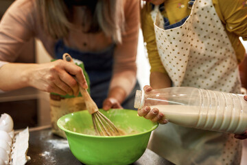 Girl pour milk in bowl while grandma mixing dough
