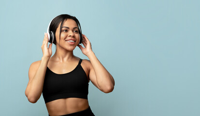 Active free time. Sporty black lady in sports uniform with headphones exercising or dancing, blue background, free space