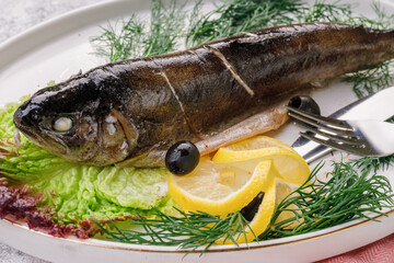 Whole baked fish. Cooked sea bass with lettuce leaves and lemon
