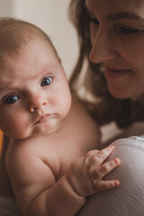 Beautiful young mother holds newborn baby girl in white lighter room at home. Tenderness cozy atmosphere