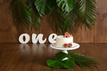 White cake with figs on a wooden stand. Tropics. Letters one