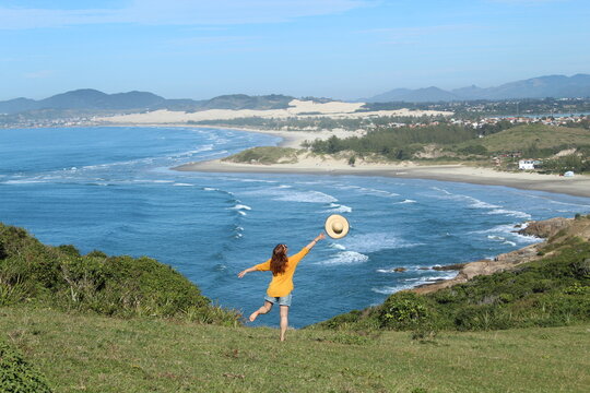 turista de roupa amarela em mirante de fente para o mar na Praia do Rosa, Santa Catarina 