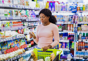 Portrait of lovely black lady checking her mobile shopping app on cellphone while buying products at big mall