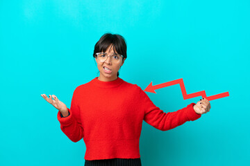 Young woman isolated on blue background holding a downward arrow and with sad expression