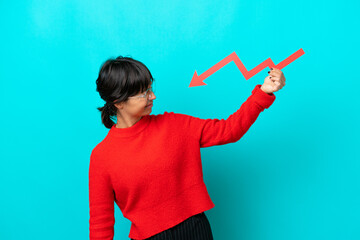 Young woman isolated on blue background holding a downward arrow and with sad expression