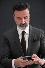 Portrait of adult businessman wearing trendy suit and sitting in modern studio on stylish chair against the black background