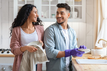Cheerful Middle Eastern Couple Sharing Domestic Chores, Washing Dishes Together In Kitchen