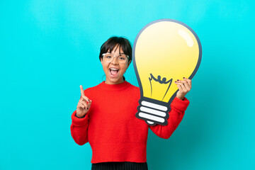 Young woman isolated on blue background holding a bulb icon and thinking