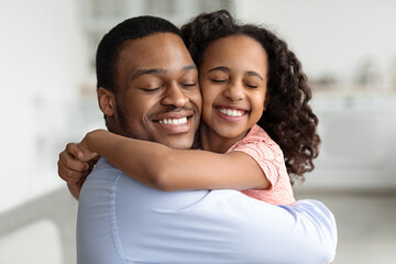 Ecstatic black father and daughter hugging with closed eyes