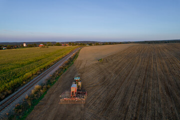 Obraz premium A green tractor plows the land near the railway. Top view. Soil preparation for sowing.