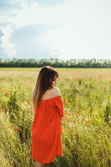 Obraz premium a girl in a red dress above the knee stands in a poppy field during the day against the sky