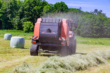 Red tractor in the field goes to the bales to collect hay.