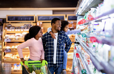 Portrait of happy black family with trolley shopping together at grocery store - obrazy, fototapety, plakaty