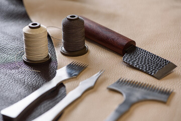Shoemaker's tools laying on piece of beige and brown genuine leather in workshop. Workplace of shoemaker for sewing handmade shoes. Selective focus