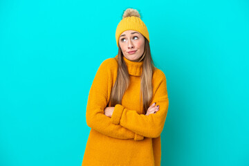 Young caucasian woman wearing winter jacket isolated on blue background making doubts gesture while lifting the shoulders