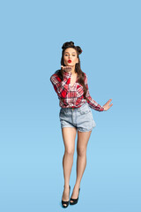 Full length portrait of sexy pinup lady in vintage style outfit blowing air kiss at camera on blue studio background