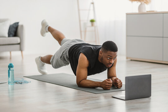 African Man Exercising At Laptop Doing Plank Leg Raises Indoor