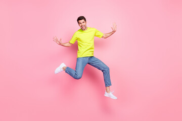 Fototapeta na wymiar Full body photo of funny brunet hairdo millennial guy jump wear green t-shirt jeans isolated on pink color background