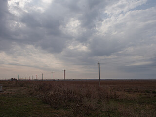 Power line poles disappearing beyand the horizon in the wild asian steppe/ Dramatic sky in grey leaden clouds