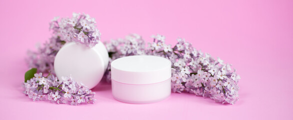 Face and body skin care. A set of cosmetic creams and balms in white tubes and cans on a coral background with sprigs of lilac flowers. Spa treatments for home care. Home rejuvenation and moisturizing