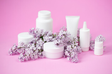 Face and body skin care. A set of cosmetic creams and balms in white tubes and cans on a coral background with sprigs of lilac flowers. Spa treatments for home care. Home rejuvenation and moisturizing