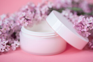 Face and body skin care. A set of cosmetic creams and balms in white tubes and cans on a coral background with sprigs of lilac flowers. Spa treatments for home care. Home rejuvenation and moisturizing