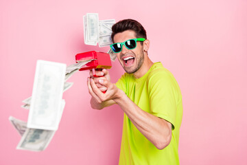 Photo portrait crazy man wearing bright t-shirt shooting with banknotes from gun isolated pastel pink color background