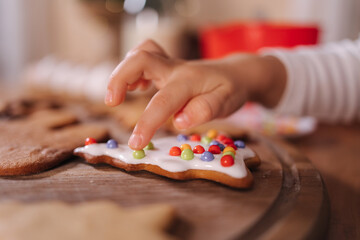 Close-up of little girl in santa hat decorates gingerbread using multicolored beads. Christmas and New Year traditions concept. Christmas bakery. Happy hollidays