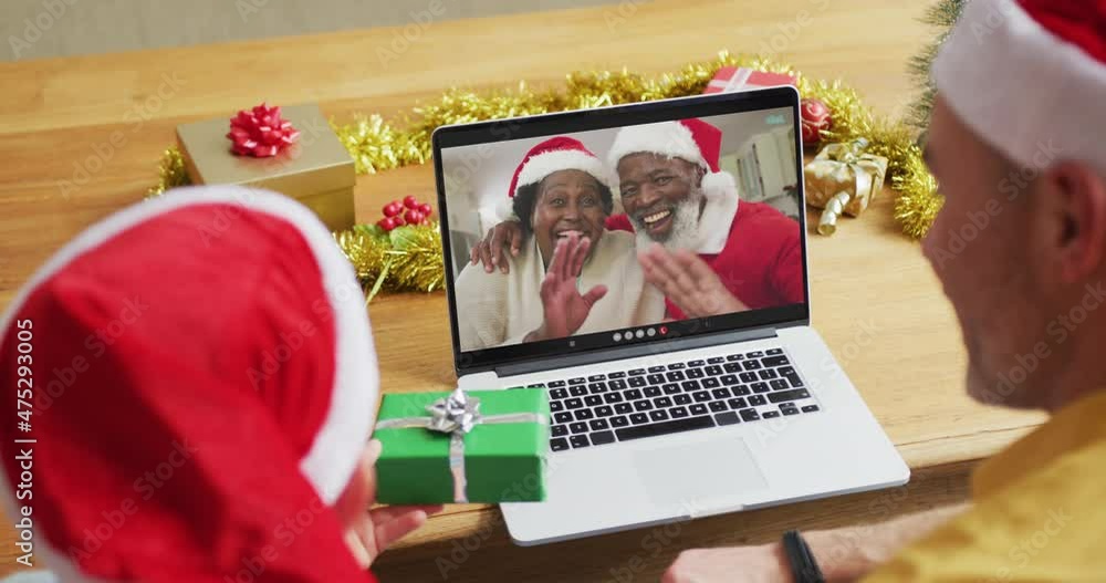 Canvas Prints Caucasian father and son with santa hats using laptop for christmas video call with couple on screen