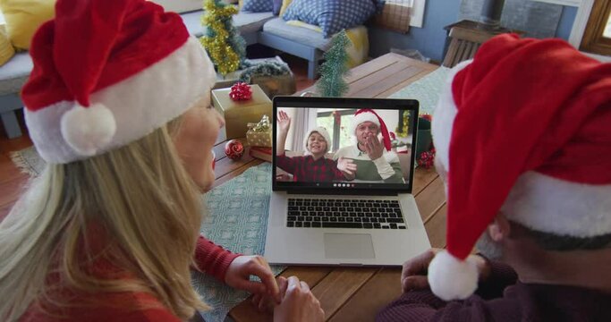Caucasian couple with santa hats using laptop for christmas video call with family on screen
