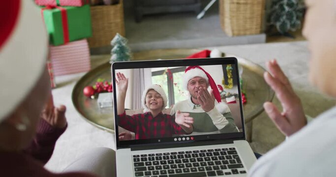 Diverse senior female friends using laptop for christmas video call with happy family on screen