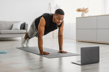 Sporty Black Guy Exercising At Laptop Doing Plank At Home