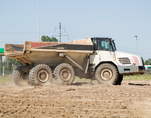 articulated dump truck in motion, driving along a dusty road. Construction machine in the process of transporting soil at a construction site © Anna