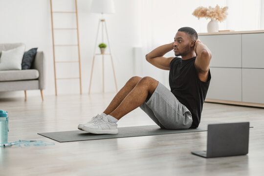 Sporty Black Man Doing Sit-Ups Exercise At Laptop Indoor, Side-View