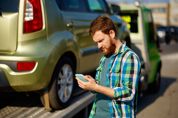 Man calling while tow truck picking up car
